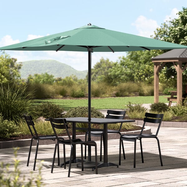 A black Lancaster Table & Seating umbrella over a table with chairs on a stone patio.