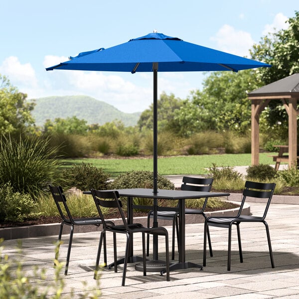 A black table and chairs on a patio with a blue Lancaster Table & Seating umbrella.