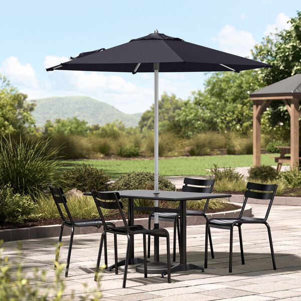 A navy Lancaster Table & Seating umbrella on a table with chairs on a patio.