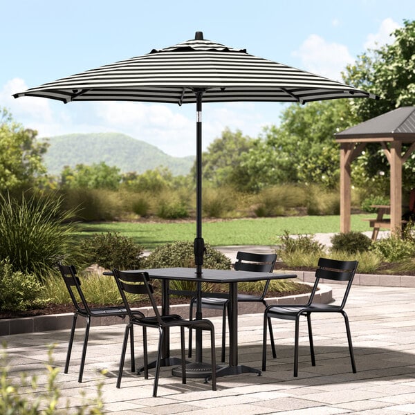 A table and chairs under a black and white striped Lancaster Table & Seating umbrella on a patio.