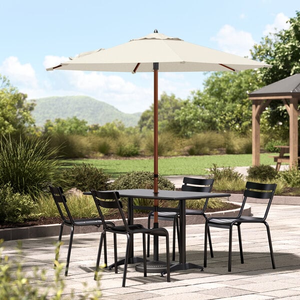 A Lancaster Table & Seating ivory umbrella on a table with chairs on an outdoor patio.