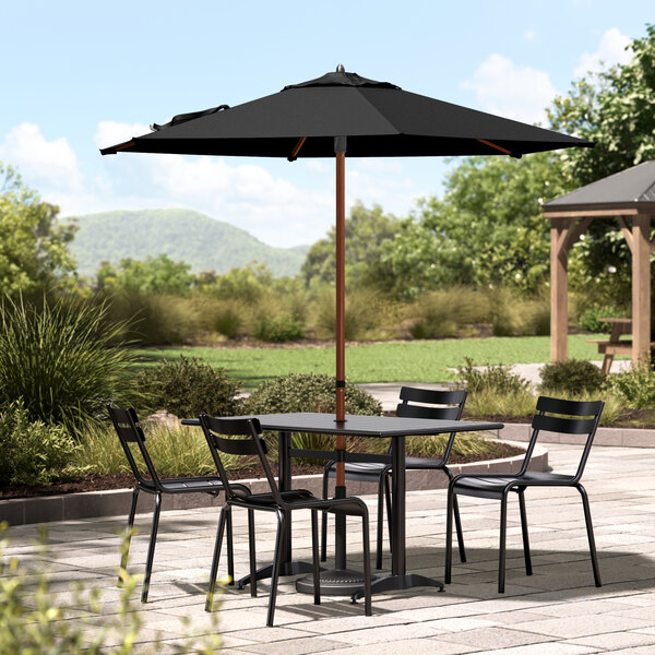 A black Lancaster Table & Seating umbrella on a patio table with chairs.