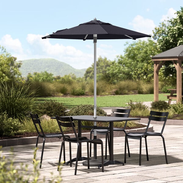 A navy Lancaster Table & Seating umbrella on a table with chairs on a stone patio.