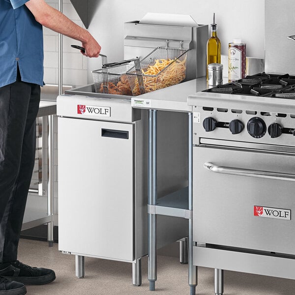 A man standing in a professional kitchen next to a white Wolf natural gas floor fryer.