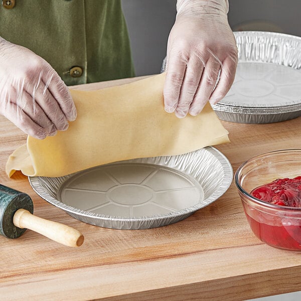 A person in a plastic glove preparing pie dough.
