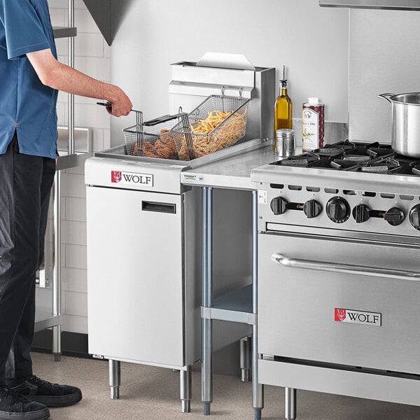 A man standing in a professional kitchen next to a Wolf natural gas floor fryer.