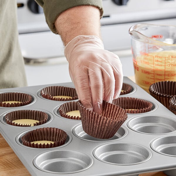 A person putting a Jumbo Glassine Baking cupcake in a muffin tin.