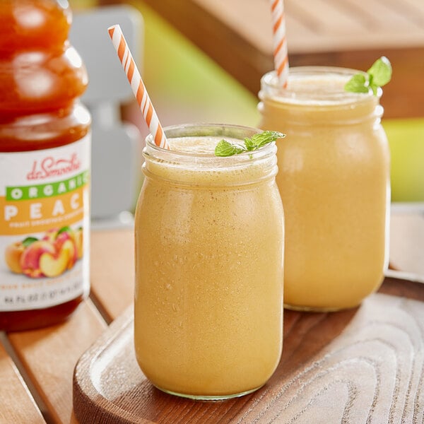 Two glass jars of Dr. Smoothie Organic Peach smoothie with straws on a table.