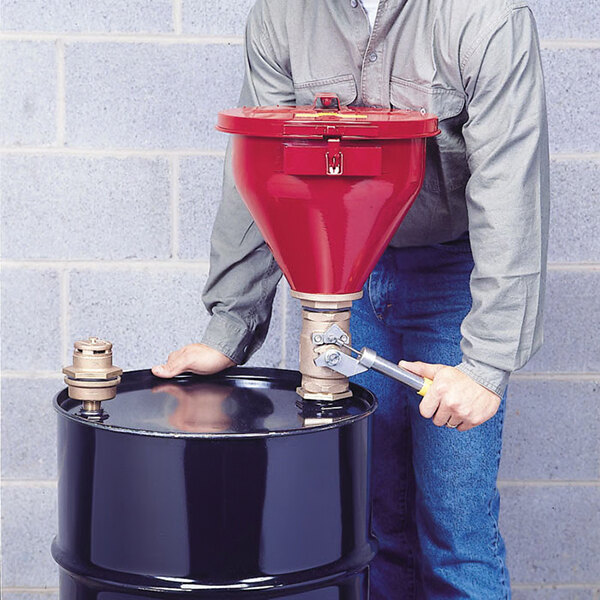 A man using a Justrite red drum funnel on a barrel.