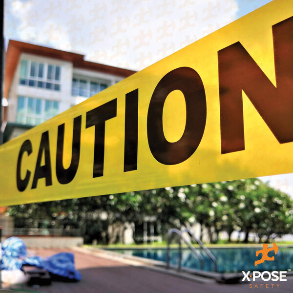 Yellow caution tape with black text reading "Caution" around a pool and a building.