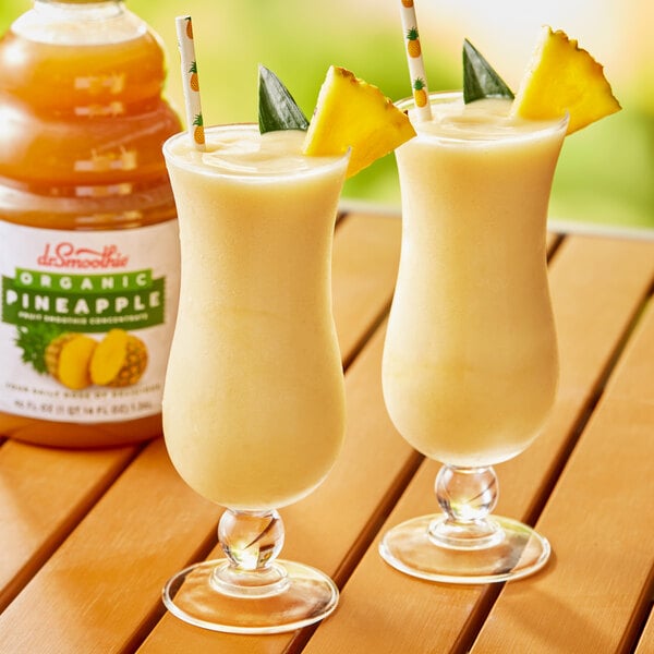 Two glasses of Dr. Smoothie Organic Pineapple smoothie on a table.