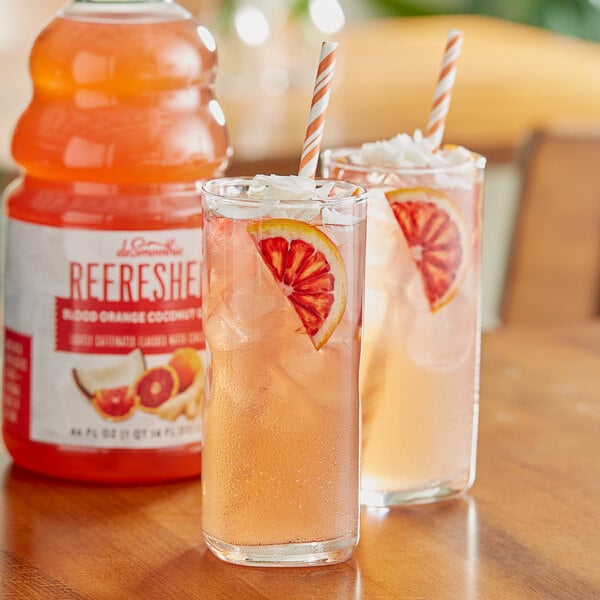 A close-up of a glass of Dr. Smoothie Blood Orange Coconut Ginger Refresher with a straw and a slice of blood orange.