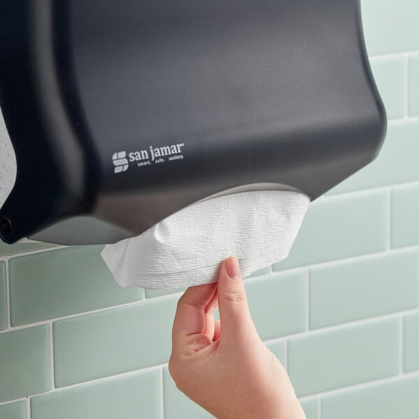 A hand pulling a white Kleenex Scottfold paper towel from a dispenser.