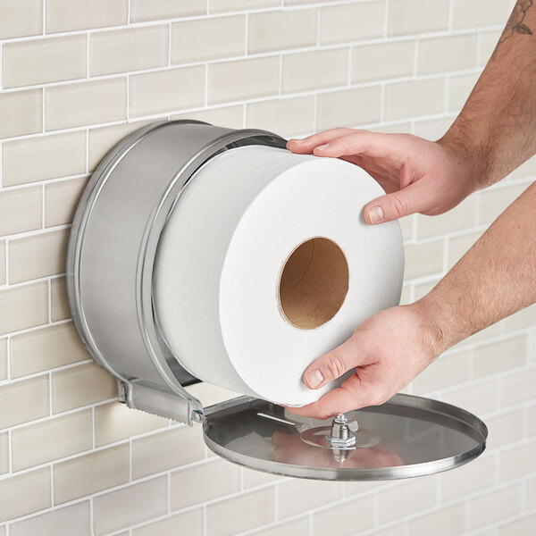 A close-up of a person's hand holding a Scott Essential jumbo toilet paper roll.