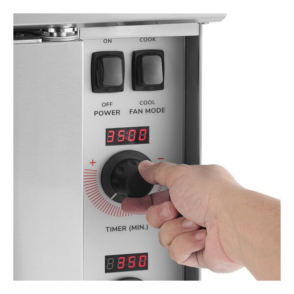 A person adjusting the timer knob on the control panel of a stainless steel electric convection oven.
