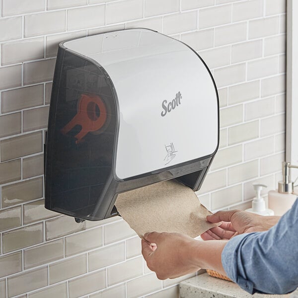 A person using a Scott Slimroll white and black automatic paper towel dispenser.