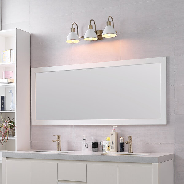 A matte brass bathroom vanity light with matte white dome shades over a mirror.