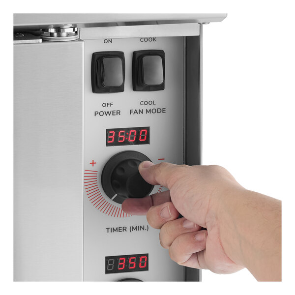 A person adjusting the timer knob on the control panel of a Cooking Performance Group double deck electric convection oven.