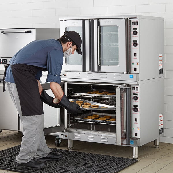 A double deck full size electric convection oven with a person placing trays of baked goods inside.