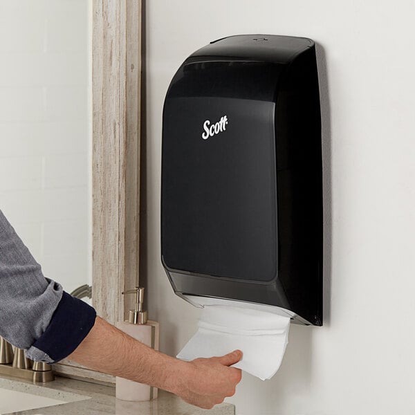 A person using a Scott black wall mount paper towel dispenser.