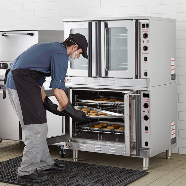 A man in a suit and hat standing in front of a Cooking Performance Group double deck commercial oven.