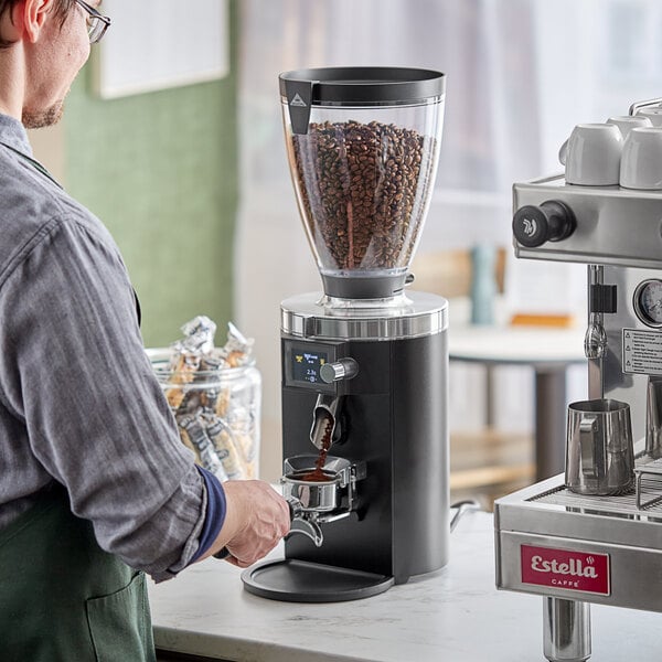 A man using a Mahlkonig black espresso grinder on a counter in a coffee shop.