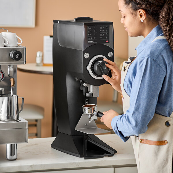 A woman using a Mahlkonig Guatemala coffee grinder on a counter.