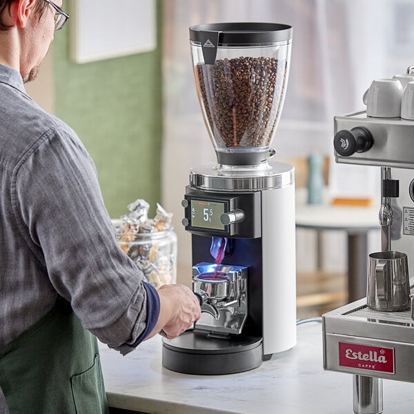 A man using a Mahlkonig white espresso grinder on a counter in a coffee shop.