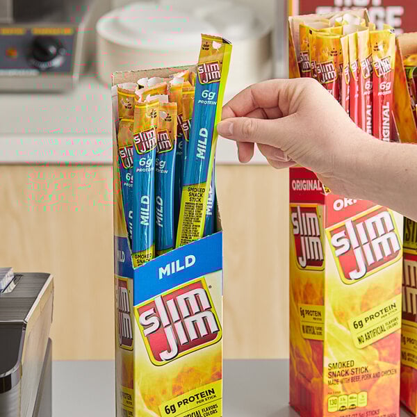 A hand holding a blue box of Slim Jim meat sticks.