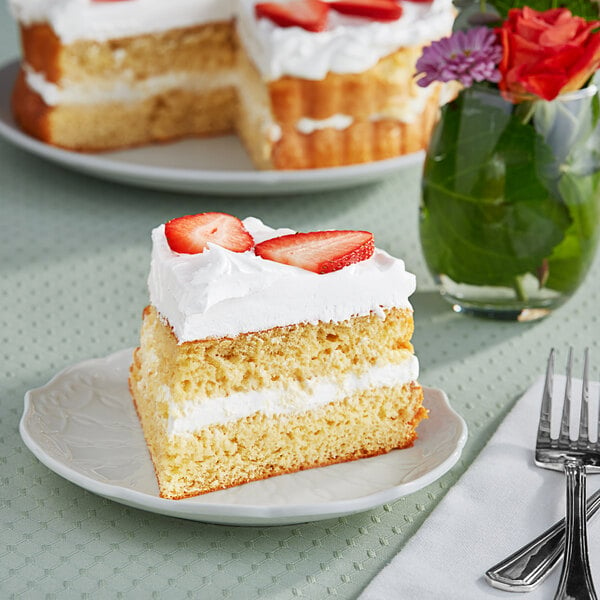 A slice of Rich's round vanilla pre-soaked sponge cake with strawberries on top on a white plate with a fork.