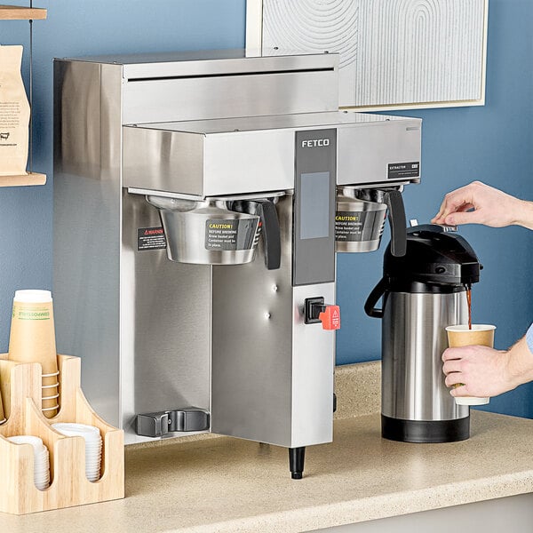 A person pouring coffee into a Fetco commercial coffee maker.