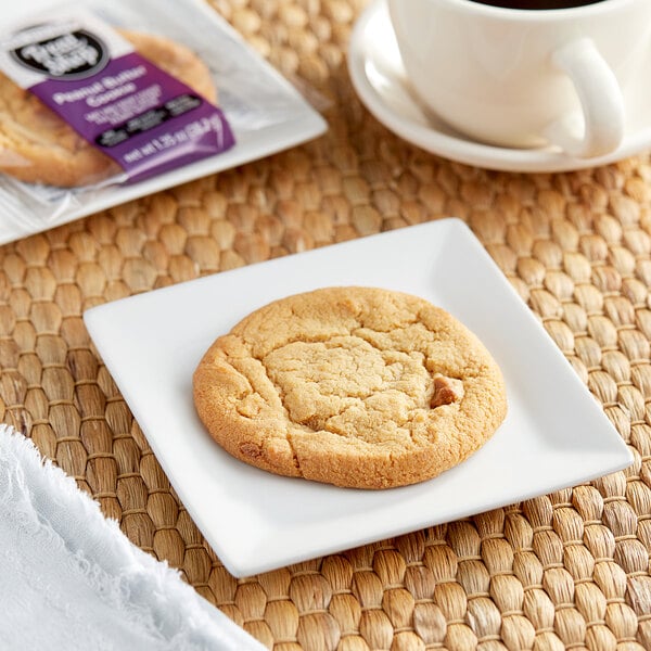 A plate of Our Specialty Treat Shop Individually Wrapped Peanut Butter Cookies next to a cup of coffee.