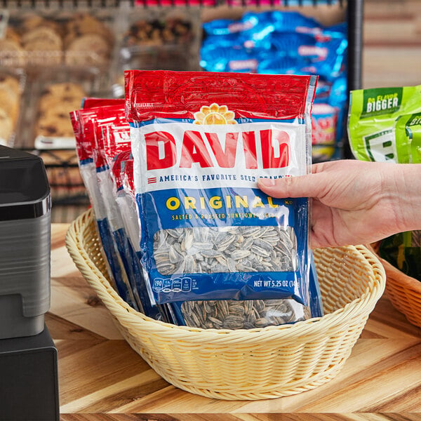 A hand holding a package of David Roasted Salted Sunflower Seeds.