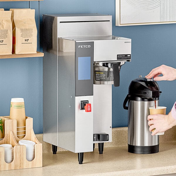 A person pouring coffee into a Fetco coffee machine.