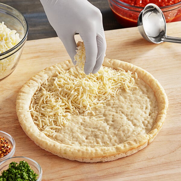 A person putting cheese on a Rich's Gluten-Free Cauliflower Pizza Crust.