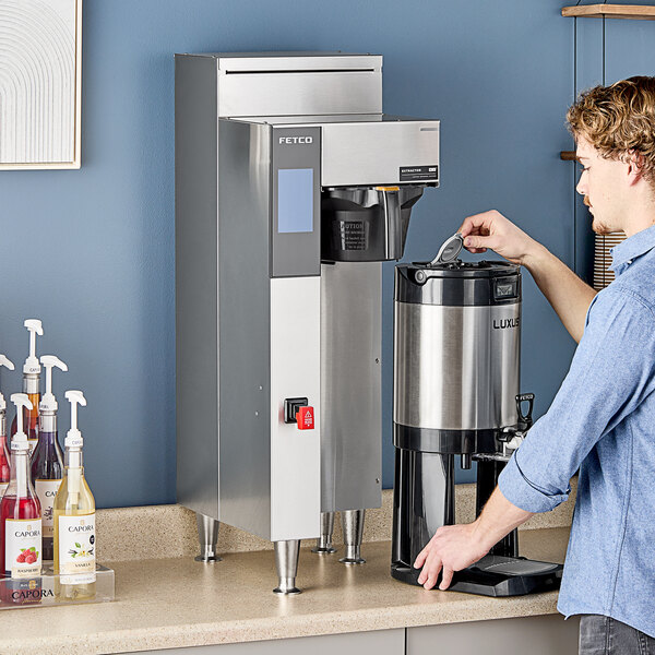 A man using a Fetco commercial coffee machine with a digital screen.