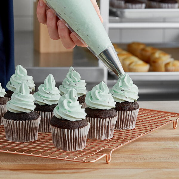 A person using a pastry bag to frost a cupcake with green Rich's Bettercreme Mint Chip frosting.