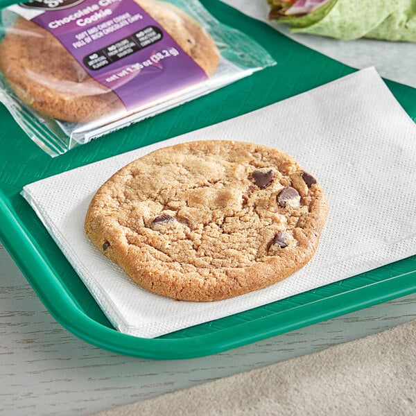 An individually wrapped Our Specialty Treat Shop chocolate chip cookie on a white napkin.