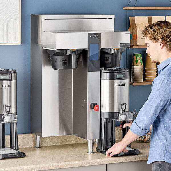 A man standing next to a Fetco twin automatic coffee machine with two black containers.