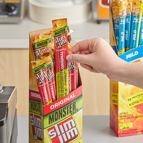 A person holding a box of Slim Jim Original Monster Meat Sticks.