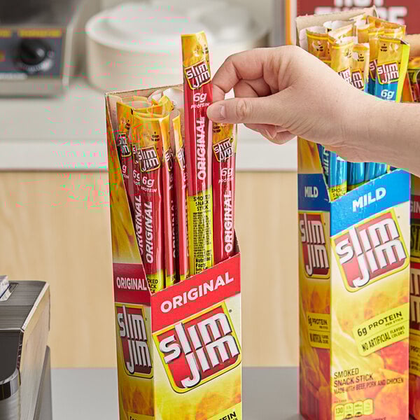 A hand holding a box of Slim Jim Original meat sticks.