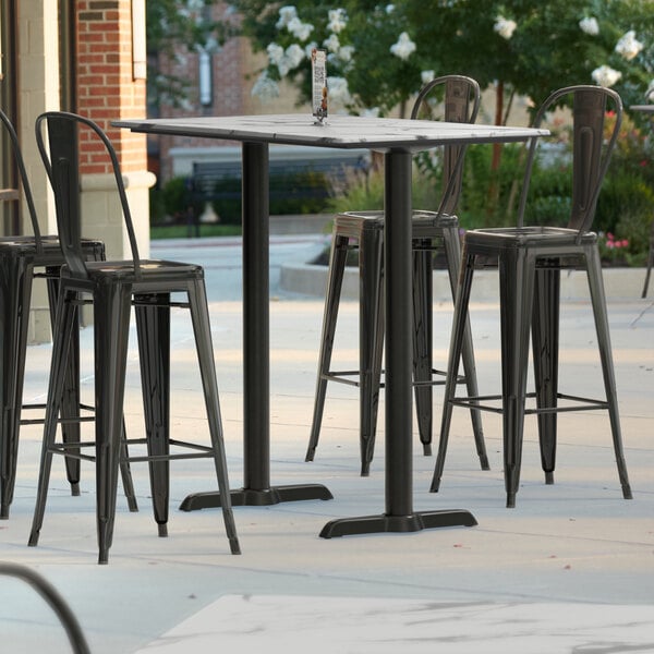 A Lancaster Table & Seating bar height table with four black bar stools on a patio.