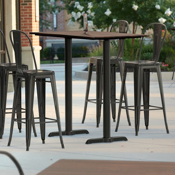 A Lancaster Table & Seating rectangular walnut bar height table with black metal chairs on a patio.