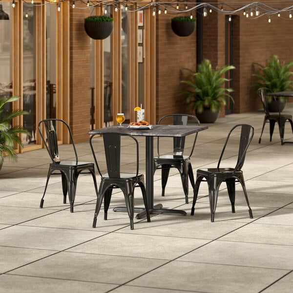 A Lancaster Table & Seating Paladina table with 4 black chairs on an outdoor patio.