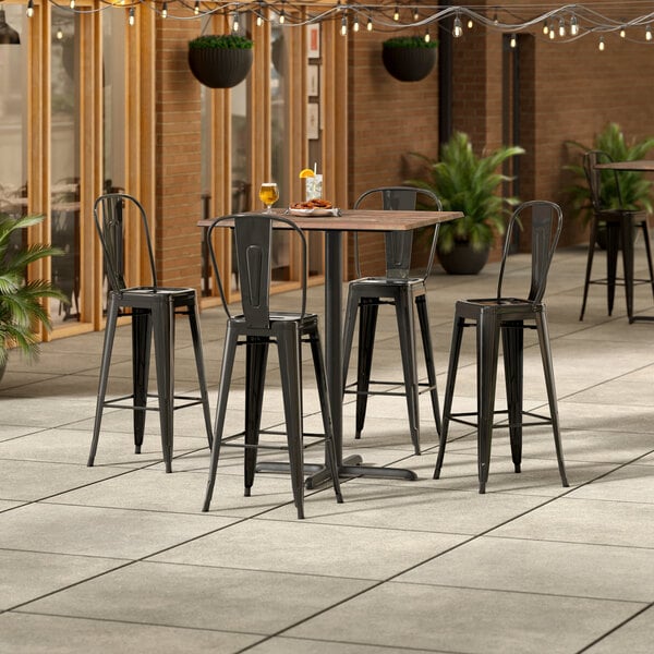 A Lancaster Table & Seating Excalibur Yukon Oak bar height table with four black chairs on a patio.