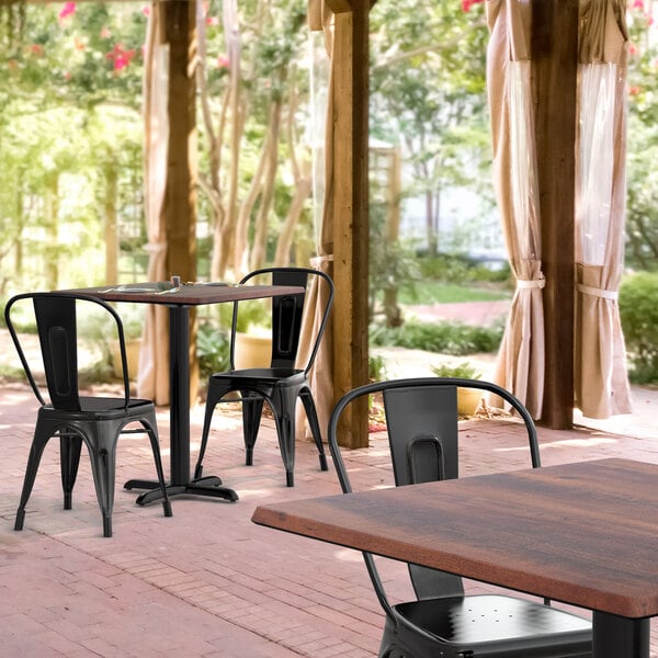 A Lancaster Table & Seating Excalibur table and chairs on a brick patio with black metal chairs.