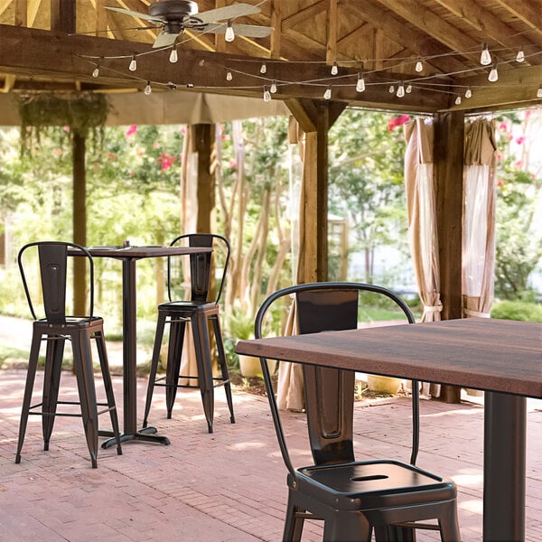 A Lancaster Table & Seating Excalibur bar height table and chairs on a covered patio.