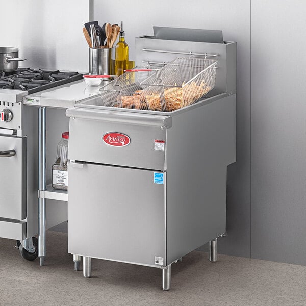 An Avantco stainless steel natural gas floor fryer with a basket of food in a commercial kitchen.