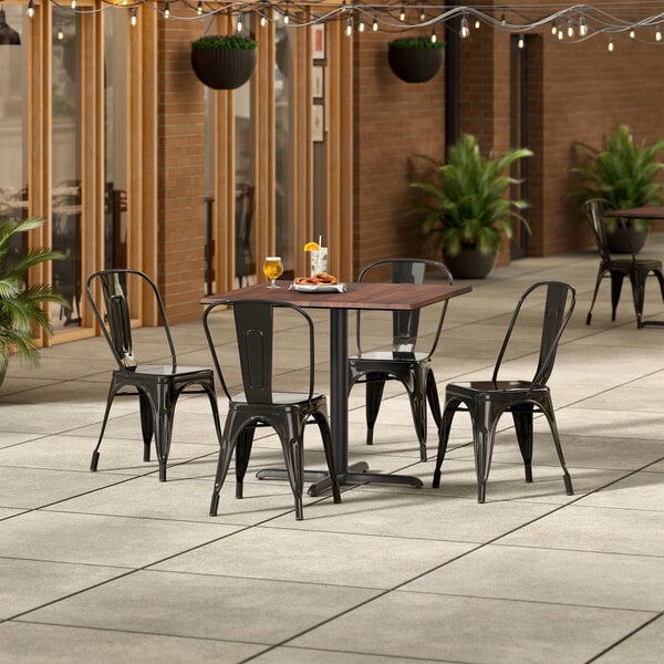 A Lancaster Table & Seating Excalibur walnut table with 4 black metal chairs on a patio.