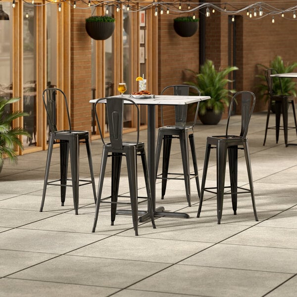 A Lancaster Table & Seating bar height table with 4 black chairs on an outdoor patio.